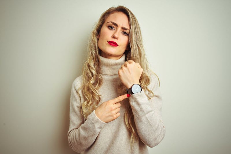 A manager is frowning while pointing to the watch on their wrist